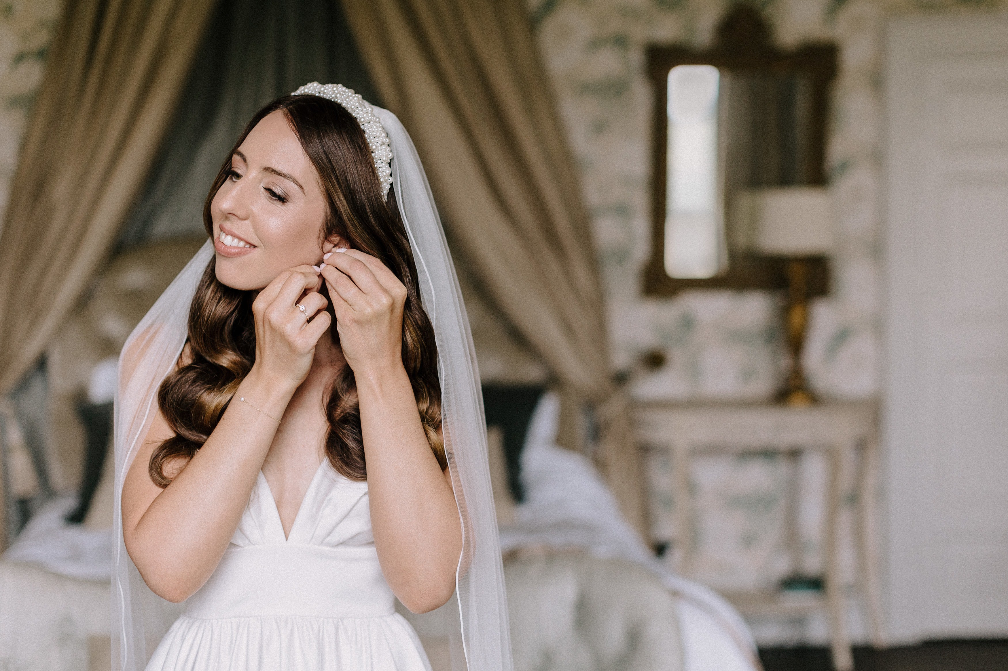 Bride in her wedding dress and veil putting in her wedding day earrings