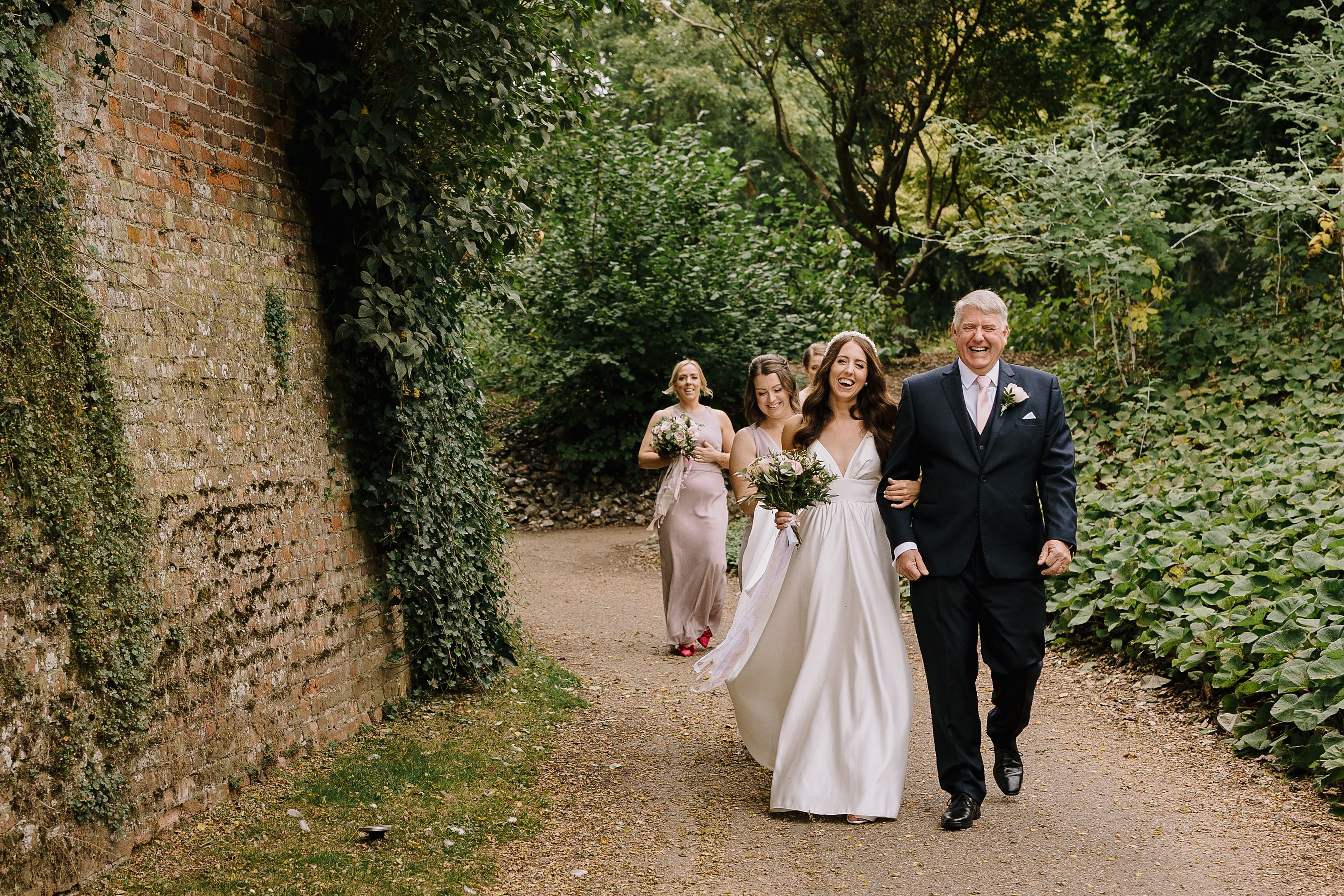 A bride with her bridesmaids and father of the bride laughing on their way to the wedding