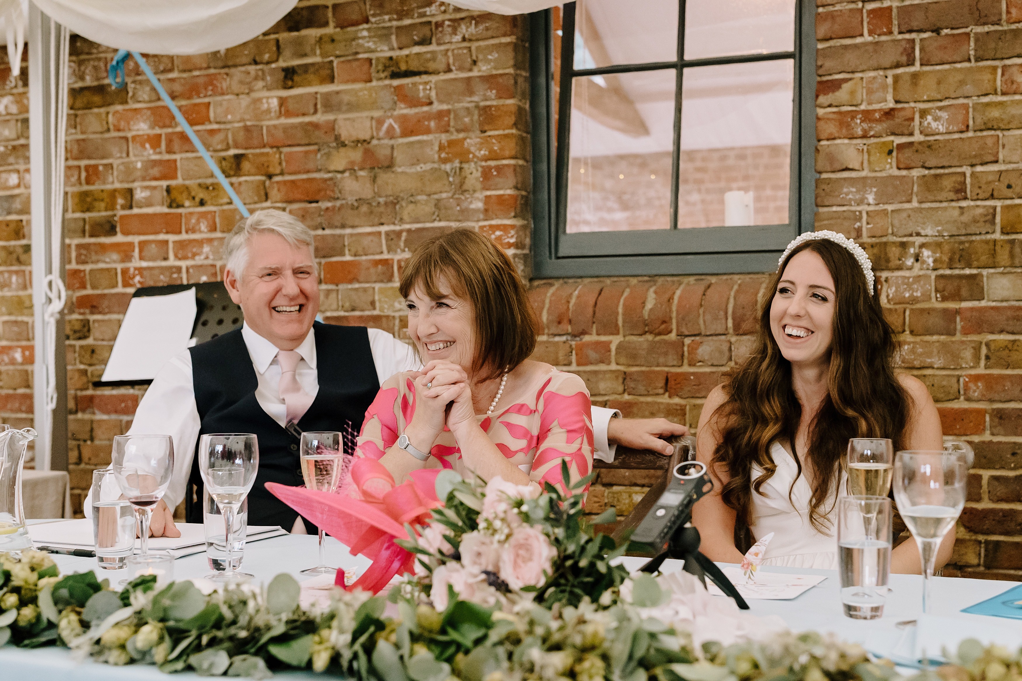 A bride and her parents laughing during a wedding speech