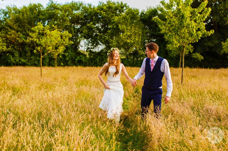 Bride and Groom walking through a field on Hendall Manor Barns ground in Uckfield